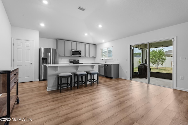 kitchen with a breakfast bar area, gray cabinetry, light wood-type flooring, a kitchen island, and stainless steel appliances