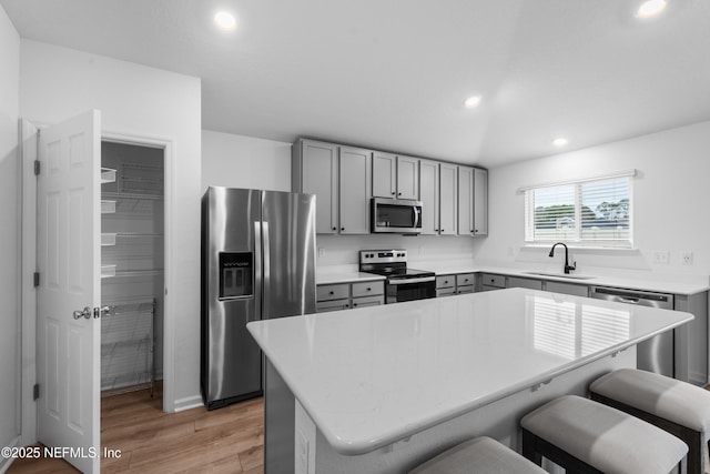 kitchen featuring appliances with stainless steel finishes, sink, a kitchen bar, a center island, and light wood-type flooring