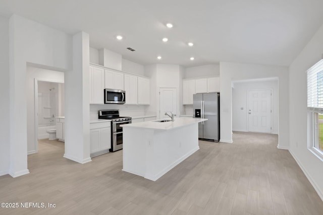 348 Salazar St, Saint Augustine, FL 32095 - kitchen featuring appliances with stainless steel finishes, a kitchen island with sink, white cabinetry, light wood-type flooring, and vaulted ceiling