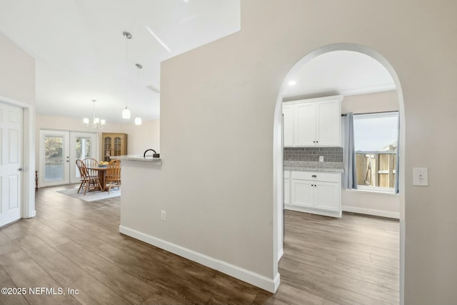 hallway with baseboards, arched walkways, wood finished floors, and a chandelier