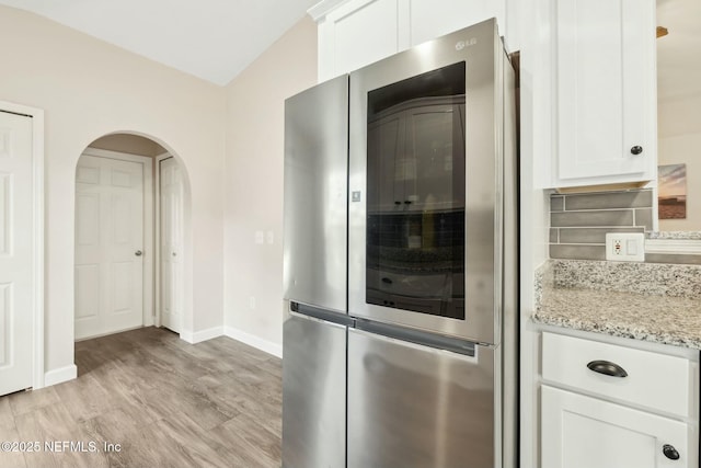 kitchen with arched walkways, white cabinets, light stone countertops, light wood-style floors, and refrigerator with glass door