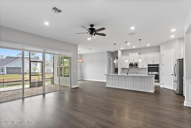 kitchen with a center island with sink, white cabinets, appliances with stainless steel finishes, decorative light fixtures, and light countertops