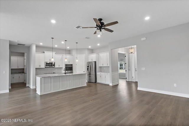 kitchen with an island with sink, appliances with stainless steel finishes, pendant lighting, and white cabinets