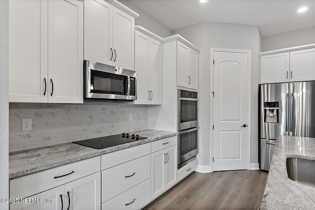 kitchen featuring light stone countertops, decorative backsplash, appliances with stainless steel finishes, white cabinetry, and wood finished floors