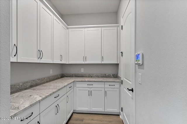 interior space with light stone counters, white cabinetry, and wood finished floors