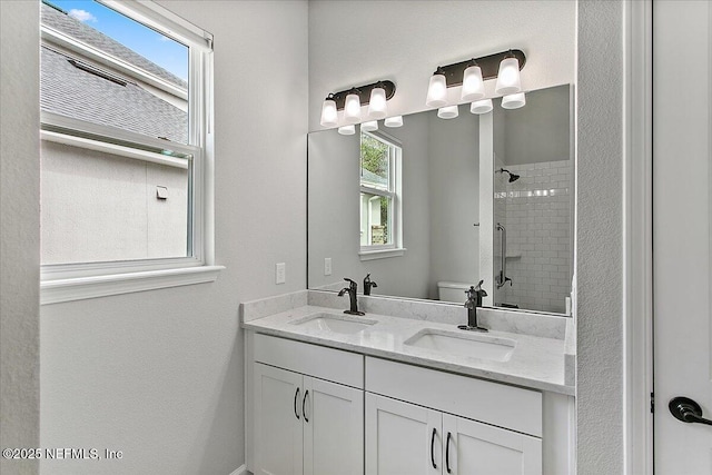 full bath featuring a tile shower, double vanity, a sink, and toilet