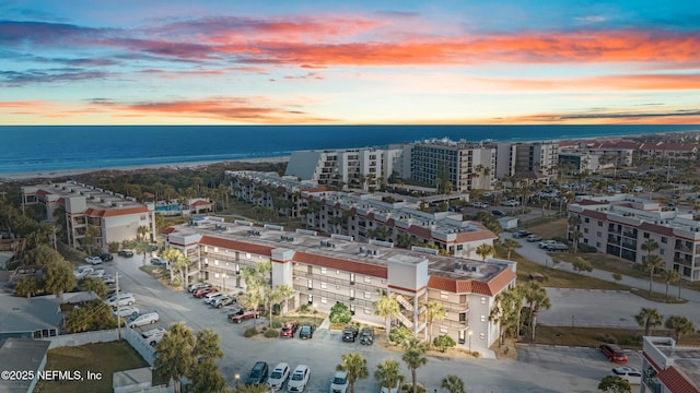 aerial view at dusk featuring a water view and a view of the beach