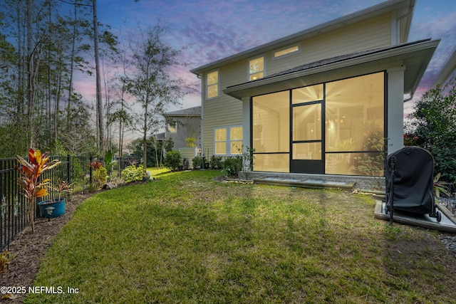 back house at dusk featuring a sunroom and a yard