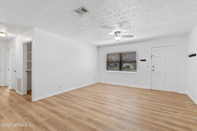 unfurnished living room featuring ceiling fan, a textured ceiling, visible vents, baseboards, and light wood-style flooring