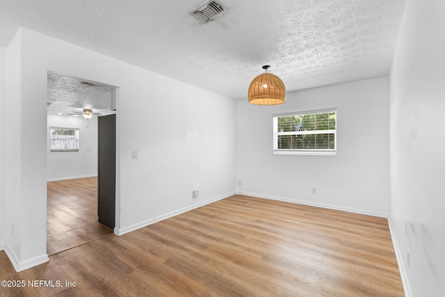 empty room featuring baseboards, a textured ceiling, visible vents, and light wood-style flooring