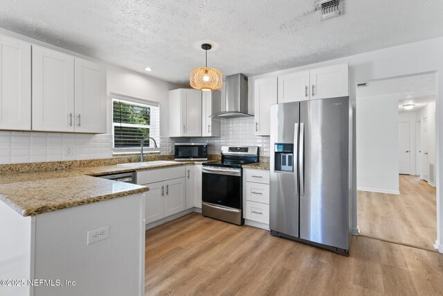kitchen featuring wall chimney range hood, visible vents, appliances with stainless steel finishes, a sink, and light wood-style flooring