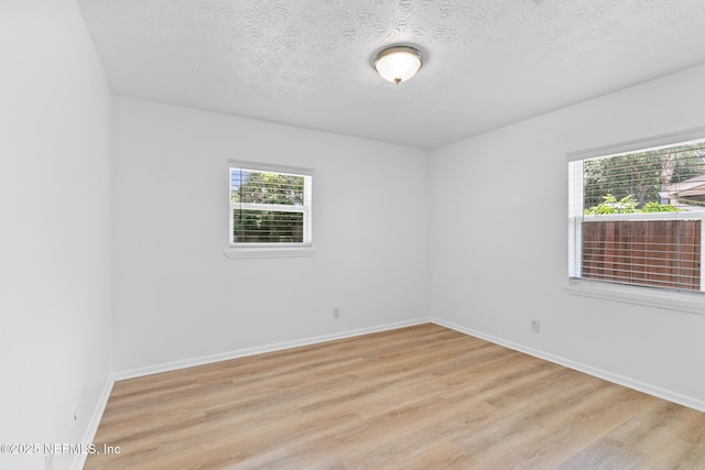 unfurnished room with a textured ceiling, baseboards, and light wood finished floors