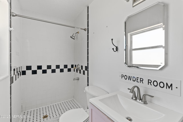 bathroom with toilet, tiled shower, and vanity