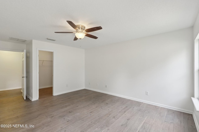 unfurnished bedroom featuring light hardwood / wood-style flooring, a walk in closet, ceiling fan, a textured ceiling, and a closet