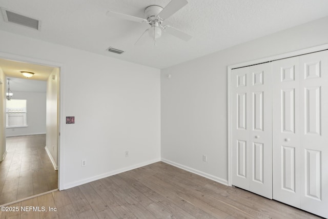 unfurnished bedroom featuring ceiling fan with notable chandelier, light hardwood / wood-style floors, a closet, and a textured ceiling
