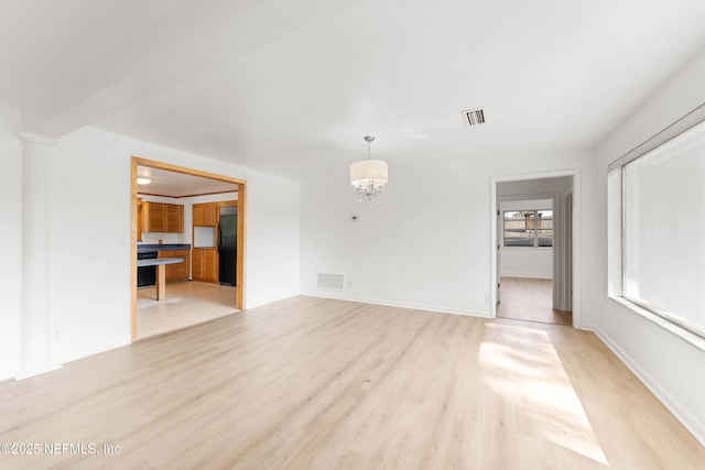 unfurnished living room featuring light wood-type flooring, visible vents, and an inviting chandelier