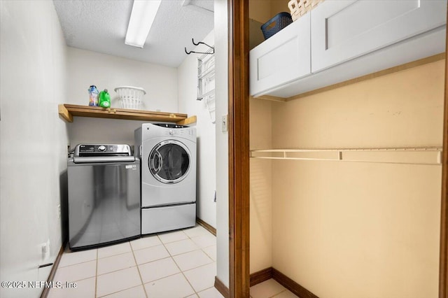 laundry area featuring cabinet space, baseboards, a textured ceiling, washing machine and dryer, and light tile patterned flooring