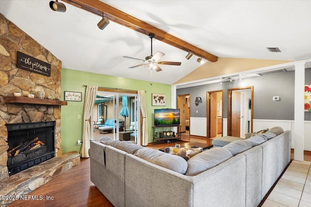 living room with vaulted ceiling with beams, a stone fireplace, wood finished floors, visible vents, and a ceiling fan