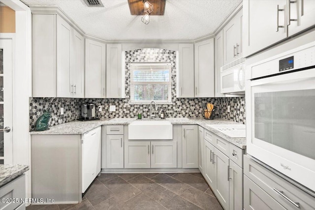 kitchen featuring white appliances, backsplash, a sink, and light stone counters