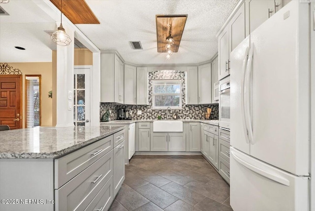 kitchen featuring white appliances, tasteful backsplash, light stone counters, hanging light fixtures, and a sink