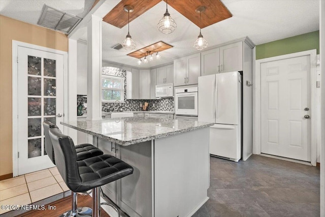 kitchen with light stone counters, a breakfast bar area, tasteful backsplash, hanging light fixtures, and white appliances