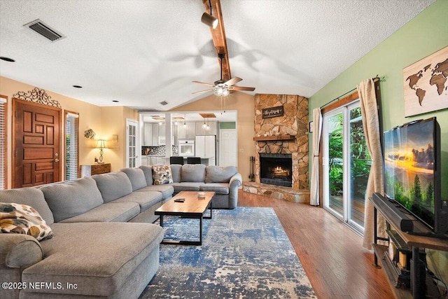 living room featuring vaulted ceiling with beams, a textured ceiling, a fireplace, wood finished floors, and visible vents