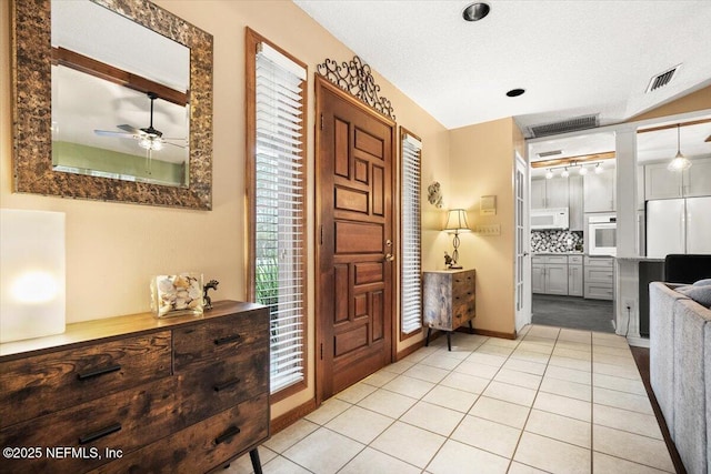 entrance foyer featuring a textured ceiling, light tile patterned flooring, visible vents, baseboards, and a ceiling fan