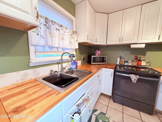 kitchen featuring butcher block countertops, white cabinetry, black electric range oven, sink, and light tile patterned floors