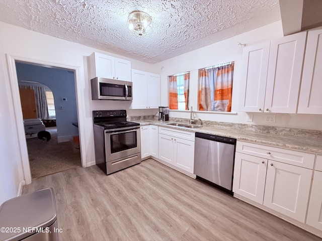 kitchen with appliances with stainless steel finishes, a wealth of natural light, sink, white cabinets, and light hardwood / wood-style floors