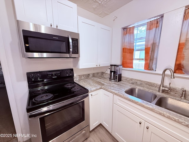 kitchen featuring sink, appliances with stainless steel finishes, light stone counters, a textured ceiling, and white cabinets