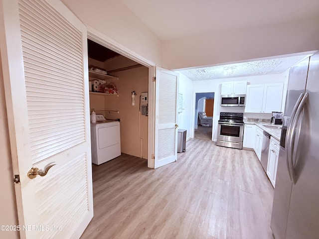 kitchen with washer / dryer, sink, white cabinetry, light wood-type flooring, and stainless steel appliances