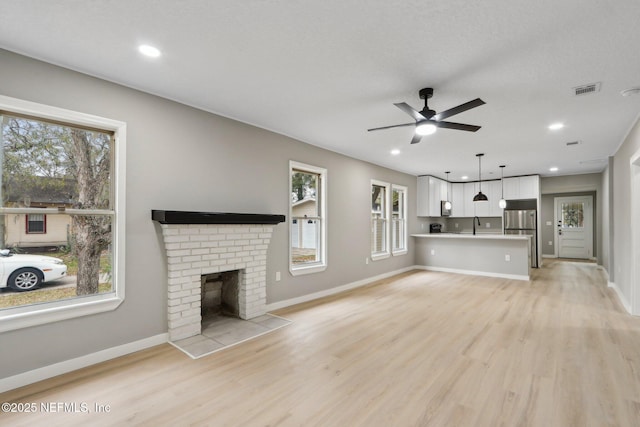 unfurnished living room featuring ceiling fan, sink, a brick fireplace, and light hardwood / wood-style flooring