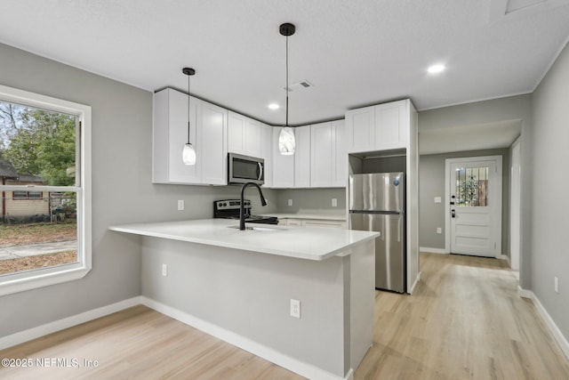 kitchen with decorative light fixtures, stainless steel appliances, kitchen peninsula, and white cabinets