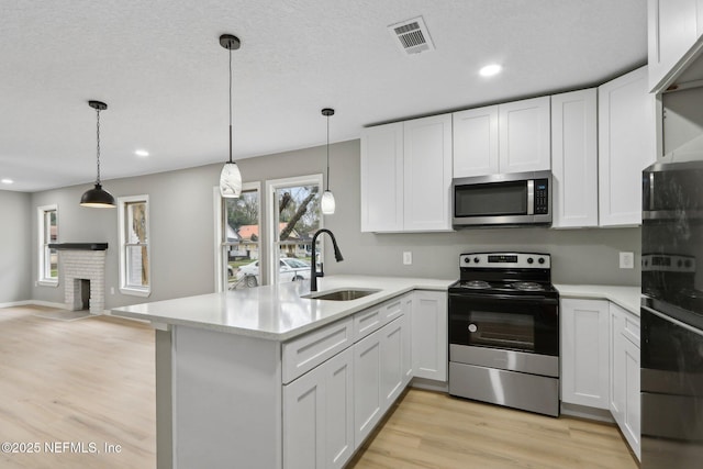 kitchen featuring sink, white cabinetry, light wood-type flooring, appliances with stainless steel finishes, and pendant lighting