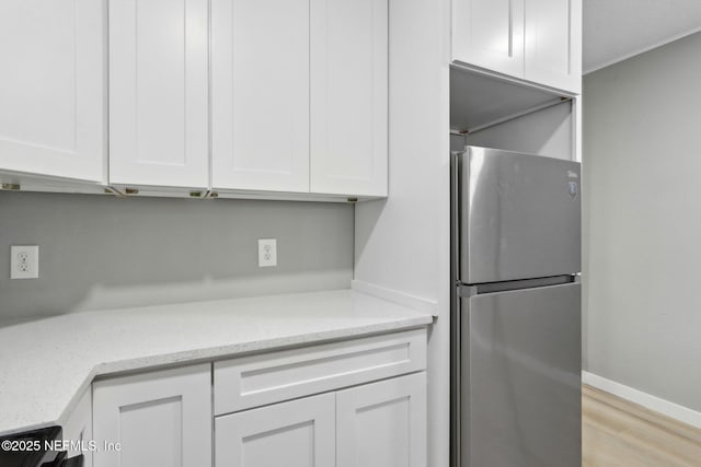 kitchen featuring white cabinetry, stainless steel fridge, light stone countertops, and light wood-type flooring