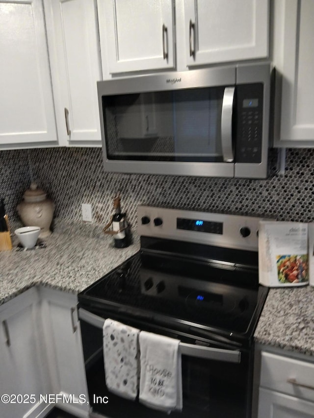 kitchen with tasteful backsplash, stainless steel microwave, white cabinets, and electric stove