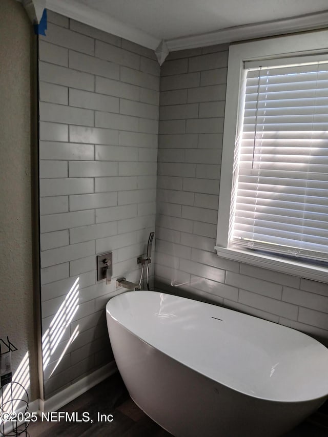 bathroom featuring a freestanding tub, tile walls, ornamental molding, and a wealth of natural light