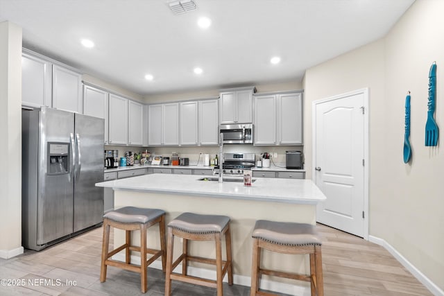 kitchen with sink, a kitchen breakfast bar, stainless steel appliances, light stone counters, and an island with sink