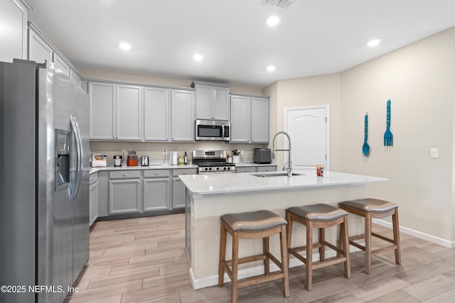 kitchen featuring sink, appliances with stainless steel finishes, a kitchen island with sink, gray cabinetry, and a kitchen breakfast bar