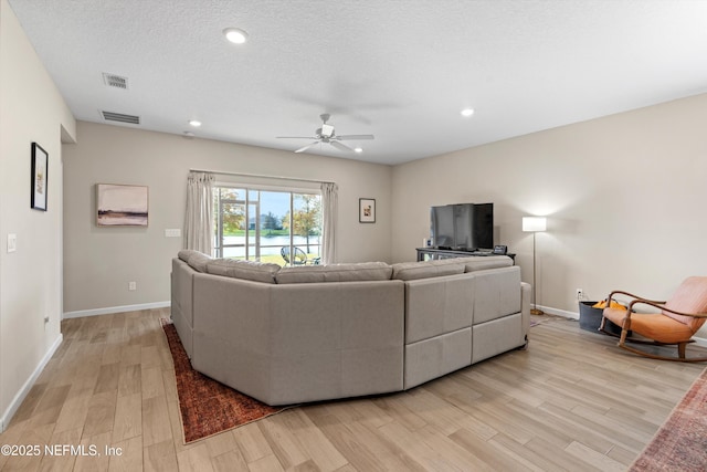 living room featuring ceiling fan, a textured ceiling, and light wood-type flooring