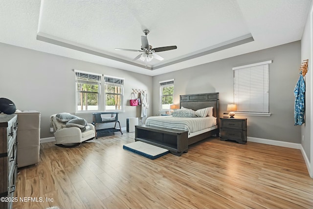 bedroom featuring baseboards, a raised ceiling, a textured ceiling, and light wood-style flooring