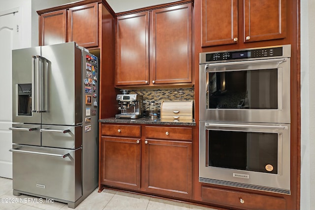 kitchen with dark stone countertops, light tile patterned floors, tasteful backsplash, and appliances with stainless steel finishes