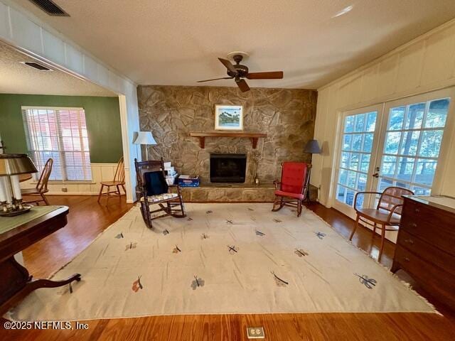 living area with a stone fireplace, hardwood / wood-style floors, ceiling fan, a textured ceiling, and french doors