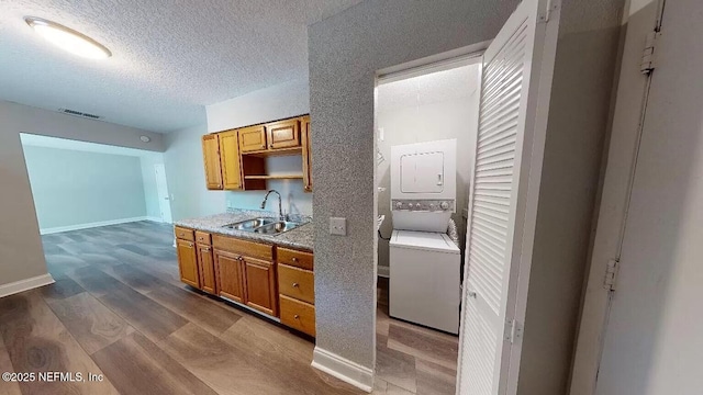 kitchen featuring sink, hardwood / wood-style floors, stacked washer and clothes dryer, and a textured ceiling