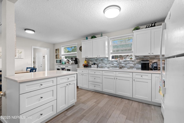 kitchen featuring tasteful backsplash, white cabinetry, sink, white fridge, and light hardwood / wood-style flooring