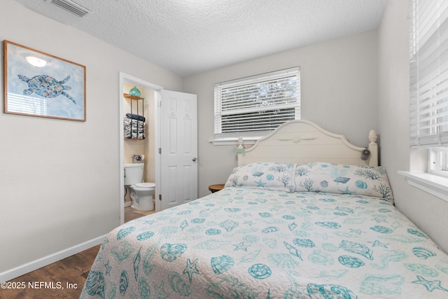 bedroom with ensuite bath, dark hardwood / wood-style flooring, and a textured ceiling