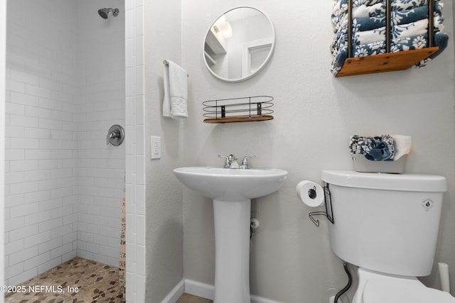 bathroom featuring tiled shower, sink, and toilet