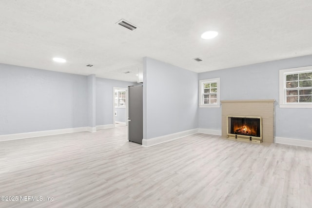 unfurnished living room with a healthy amount of sunlight, a brick fireplace, light hardwood / wood-style flooring, and a textured ceiling