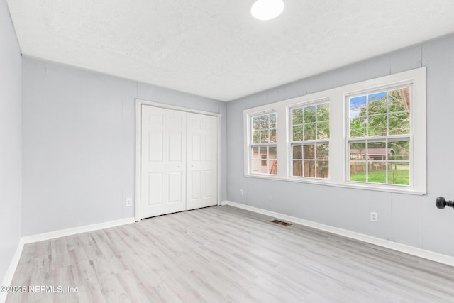 unfurnished bedroom with light hardwood / wood-style floors, a closet, and a textured ceiling