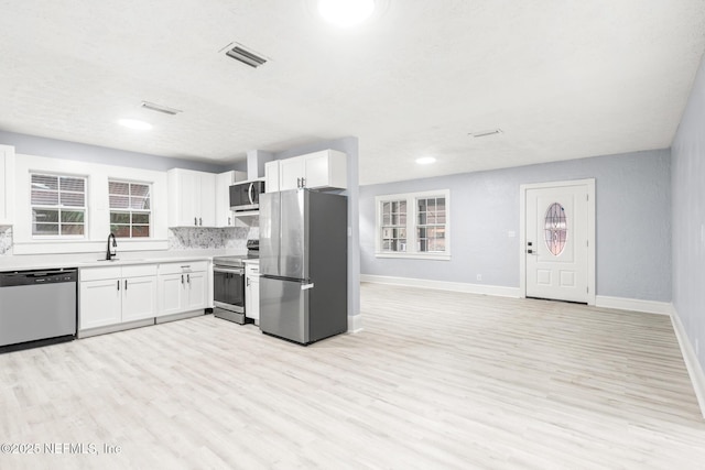 kitchen with tasteful backsplash, white cabinetry, sink, stainless steel appliances, and light wood-type flooring